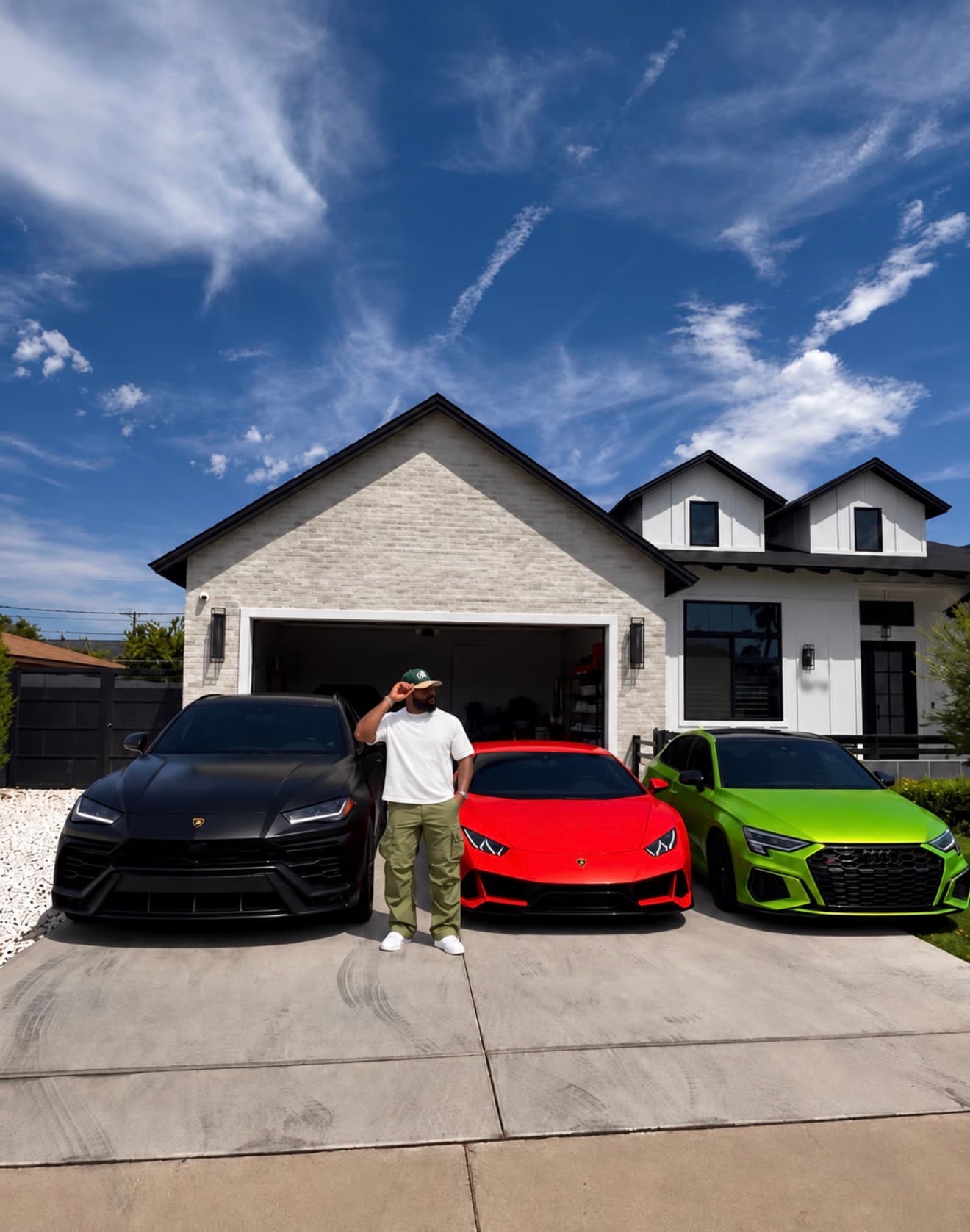 Solo E standing in front of his home beside a black Lamborghini Urus, red Lamborghini Huracán, and green Audi RS3